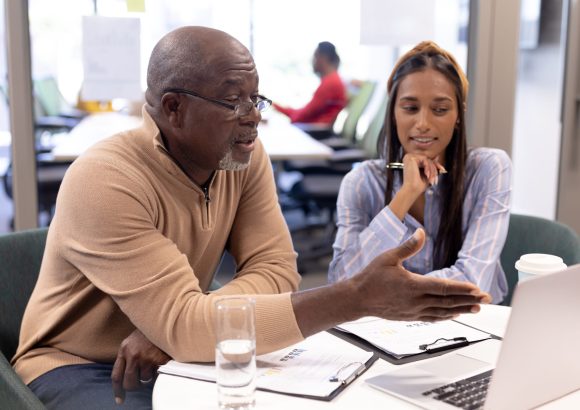 African american businessman discussing over laptop with biracial businesswoman at modern workplace. unaltered, business, teamwork, modern office and technology concept.