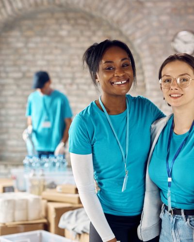 African American woman and her Caucasian friend working as volunteers at humanitarian aid center and looking at camera.